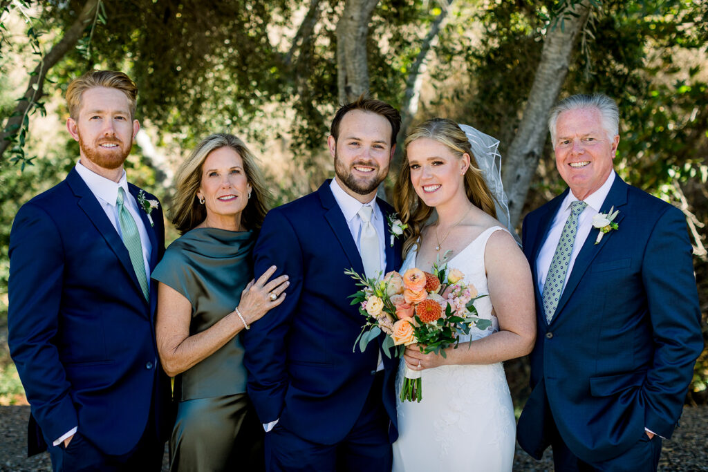 A heartwarming family photo featuring the bride and groom on their wedding day at Higuera Ranch. The couple is surrounded by loved ones, sharing smiles and joy, capturing a beautiful moment of togetherness amidst the rustic charm of the ranch setting.